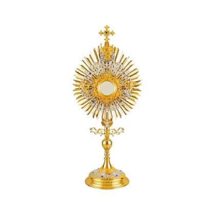 Brass monstrance in traditional style, 24-karat gold-plated with silver-plated accents, decorated with blue stones. The glory consists of three layers: a sunburst and two floral wreaths made of open filigrees. The bigger wreath has figures of God the Father and Jesus attached to the top, and figures of angels placed on both sides of the luna case. Below the sunburst there is an image of the Dove (the Holy Spirit) surrounded by rays.