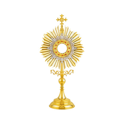 Traditional, sun-shaped monstrance made of brass, 24-karat gold-plated. The luna case is surrounded by a silver-plated floral wreath and a round decorative frame set with red stones. At the top of the monstrance there is a big cross with sculpted ornaments. The node and the base are finished in high gloss.