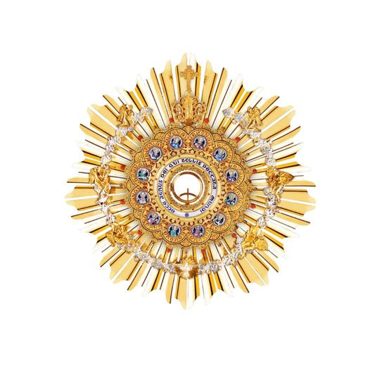 Brass hanging monstrance, 24-karat gold-plated with red stones and enameled accents, inspired by German models from the late XIX and early XX centuries. The magnificent glory consists of a sunburst and a layer of ornate open filigrees with medallions depicting the Apostles. The gold-rimmed luna case has a blue-enameled Latin inscription: “Ecce Agnus dei Qui Tollis Peccata Mundi”. The stem and the node are decorated with fine filigrees. Medallions on the round base feature symbols of the Evangelists. All med