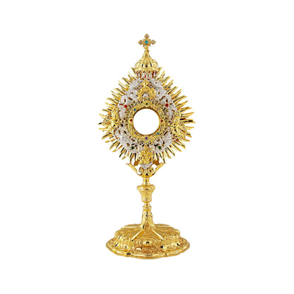 Richly adorned Baroque brass monstrance, 24-karat gold-plated with silver-plated accents. The glory consists of three layers: two sunbursts topped with a cross and a silver-plated wreath. The wreath features angel figures on either side of the luna case and God the Father sheltered with a canopy right above it. The luna case is surrounded by an ornamental design set with colorful stones. Highly decorated, sculpted node and base.
