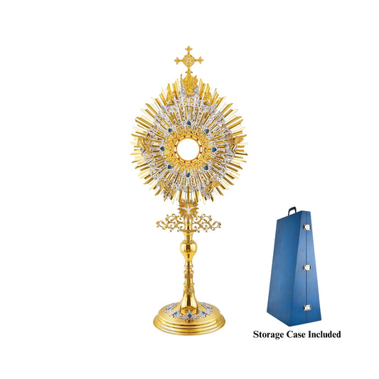 A large monstrance (height: 43-3/4") made of brass, 24-karat gold-plated with silver-plated and blue-enameled accents. The sunburst-shaped glory consists of three layers of rays and two silver-plated wreaths made of ornate floral scrollwork. The bigger wreath is adorned with figures of God the Father and Jesus at the top, and six angels around the luna case. The opening for the luna is gold-rimmed, filigreed and encrusted with synthetic red gemstones. 
