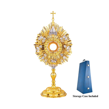 Eclectic brass monstrance, 24-karat gold plated, in the lightly pointed form topped by a cross. A wreath of grapevine leaves and crops adorns the sunburst glory. There are images of God the Father at the top and the Lamb of God at the bottom of the wreath. Equipped with a round luna graced with a floral motif. A decorative pattern of leaves set with red stones surrounds the luna case. Both the base and the nodus are richly embellished.