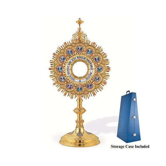Brass monstrance, 24-karat gold-plated with red stones and enameled accents, inspired by German models from the late XIX and early XX centuries. The magnificent glory consists of a sunburst and a layer of ornate open filigrees with medallions depicting the Apostles. The gold-rimmed luna case has a blue-enameled Latin inscription: “Ecce Agnus dei Qui Tollis Peccata Mundi”. The stem and the node are decorated with fine filigrees. Medallions on the round base feature symbols of the Evangelists. 