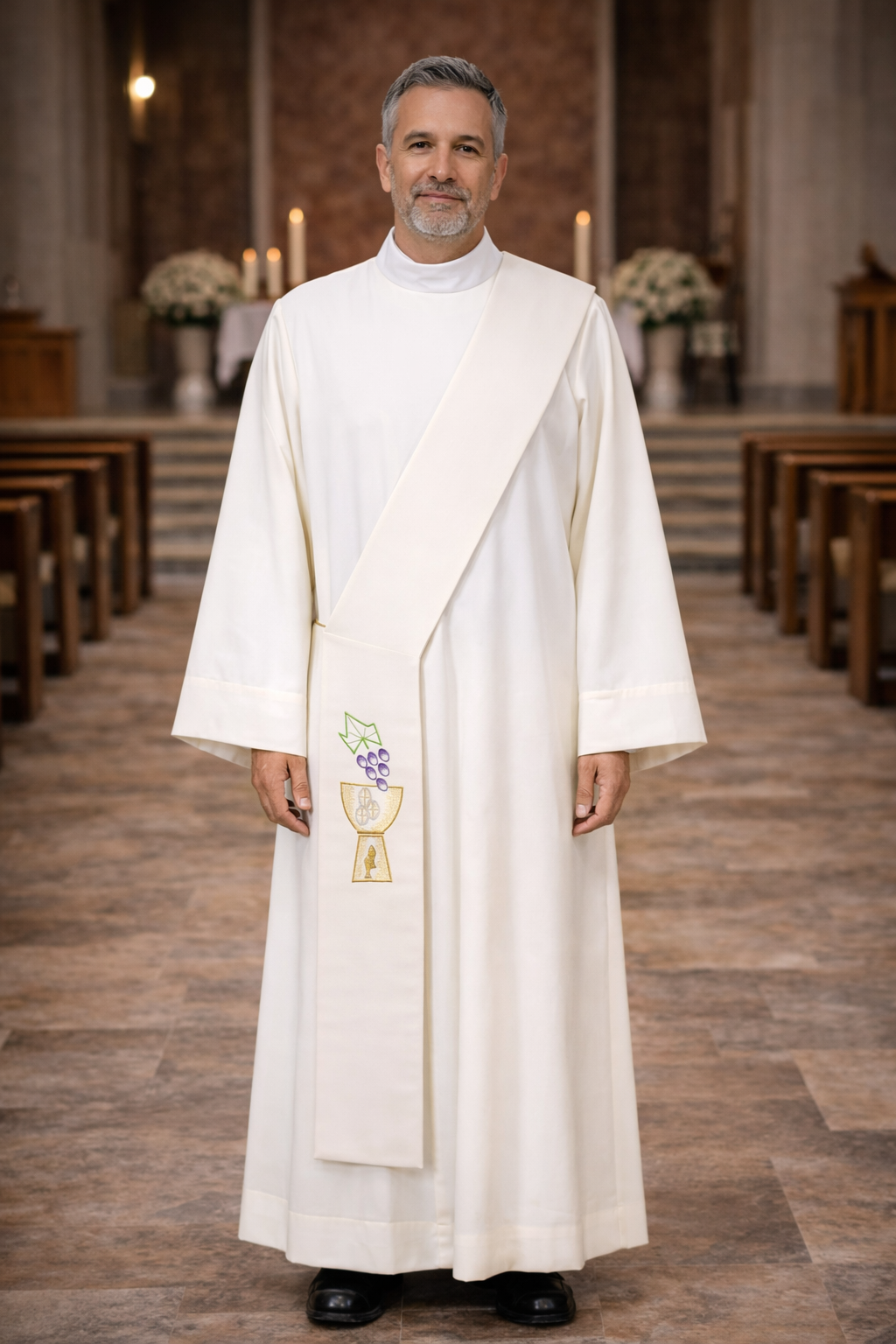 Deacon in white alb with ivory stole with chalice and grapes design standing in a church.