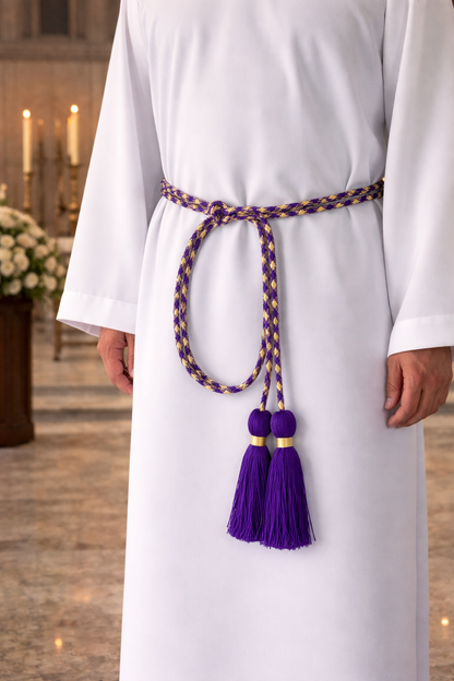 Clergy wearing a white alb with a decorative cinture featuring tassels in an indoor setting.
