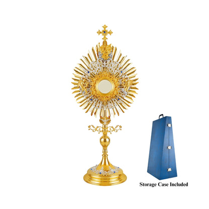 Brass monstrance in traditional style, 24-karat gold-plated with silver-plated accents, decorated with blue stones. The glory consists of three layers: a sunburst and two floral wreaths made of open filigrees. The bigger wreath has figures of God the Father and Jesus attached to the top, and figures of angels placed on both sides of the luna case. Below the sunburst there is an image of the Dove (the Holy Spirit) surrounded by rays.