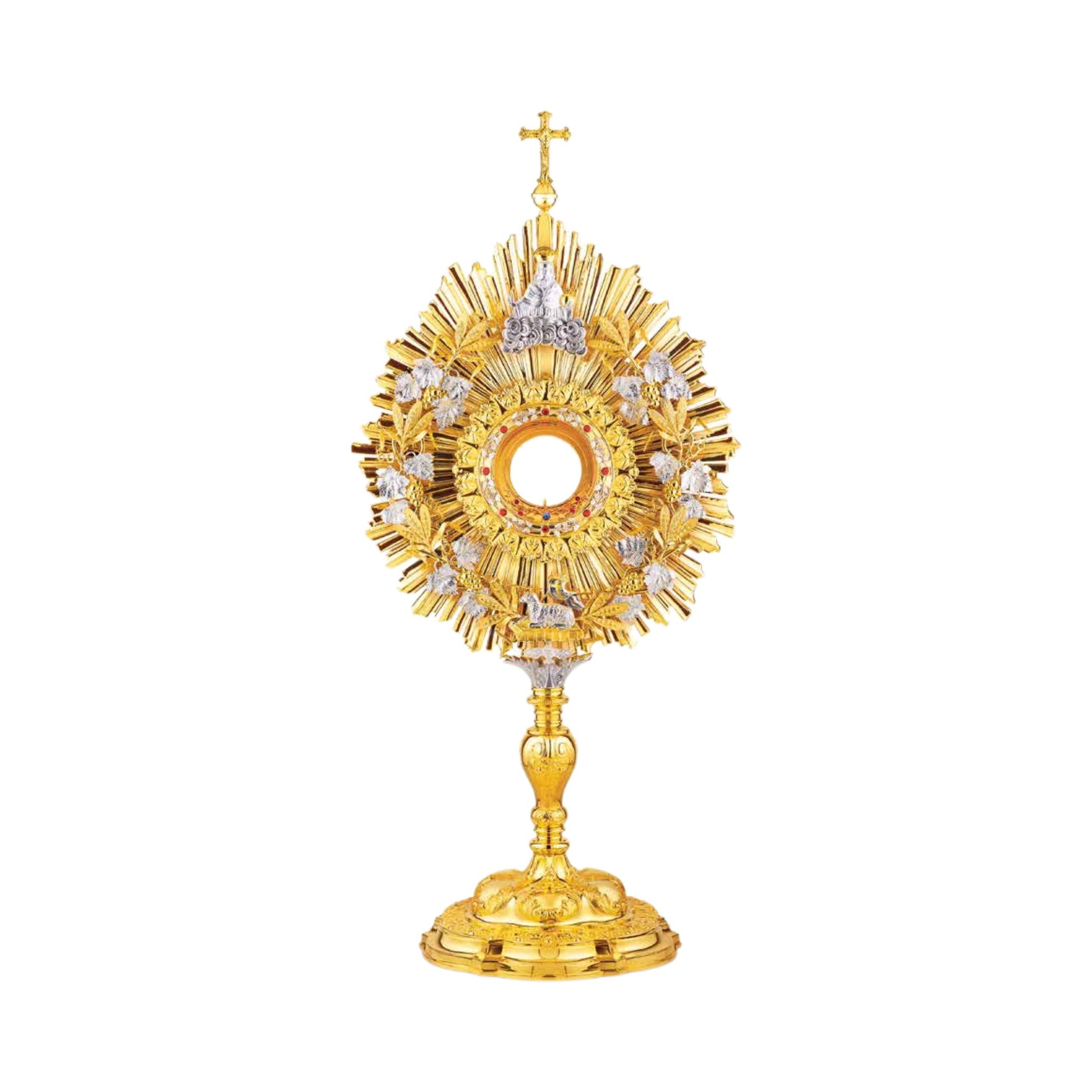 Eclectic brass monstrance, 24-karat gold plated, in the lightly pointed form topped by a cross. A wreath of grapevine leaves and crops adorns the sunburst glory. There are images of God the Father at the top and the Lamb of God at the bottom of the wreath. Equipped with a round luna graced with a floral motif. A decorative pattern of leaves set with red stones surrounds the luna case. Both the base and the nodus are richly embellished.